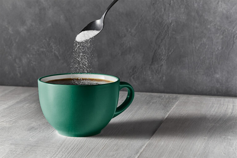 sugar pouring from a spoon into coffee in a mug